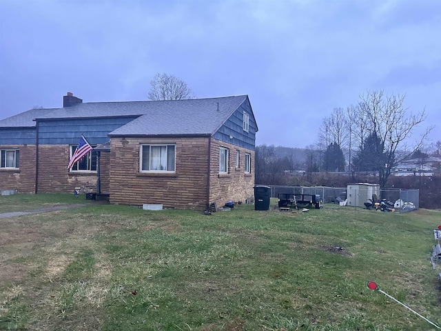 view of side of home with a yard, a shingled roof, a chimney, and fence