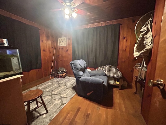 sitting room with hardwood / wood-style flooring, ceiling fan, and wood walls