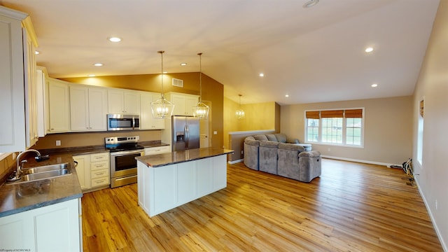 kitchen featuring lofted ceiling, sink, appliances with stainless steel finishes, decorative light fixtures, and a kitchen island