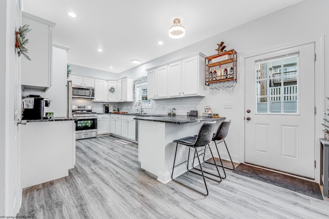 kitchen featuring kitchen peninsula, stainless steel appliances, dark stone countertops, white cabinetry, and a breakfast bar area