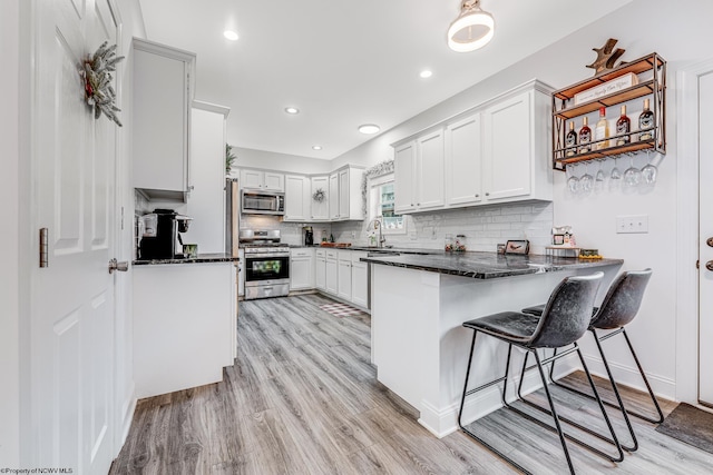 kitchen with white cabinetry, tasteful backsplash, kitchen peninsula, dark stone countertops, and appliances with stainless steel finishes