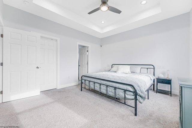 carpeted bedroom with ceiling fan, a raised ceiling, and a closet