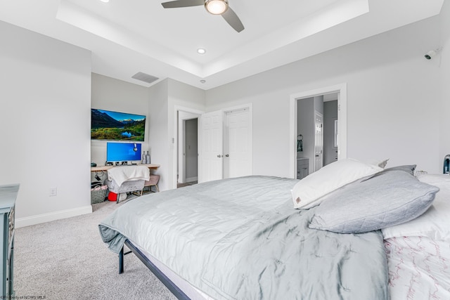 carpeted bedroom featuring ceiling fan, a raised ceiling, and ensuite bath