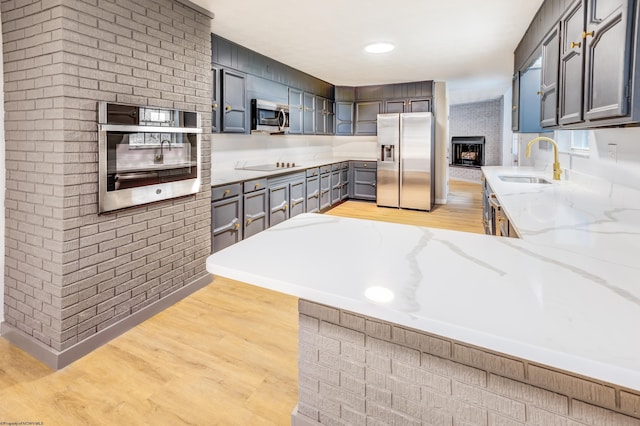 kitchen with sink, light stone counters, kitchen peninsula, light hardwood / wood-style floors, and appliances with stainless steel finishes