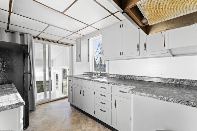 kitchen with white cabinets, a paneled ceiling, black refrigerator, and sink