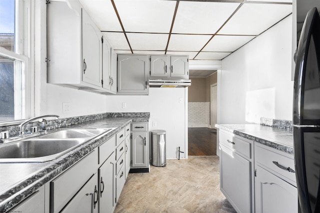 kitchen featuring sink, black fridge, ventilation hood, gray cabinets, and a paneled ceiling