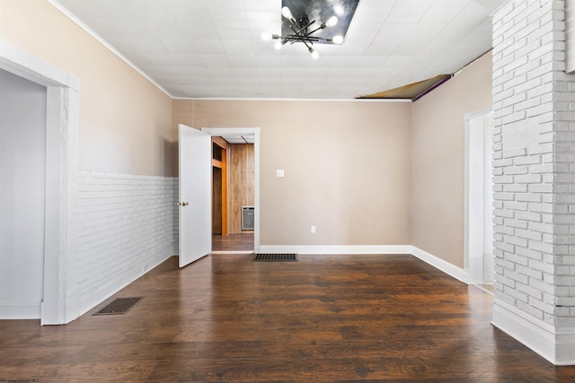 empty room with dark hardwood / wood-style flooring, crown molding, and brick wall