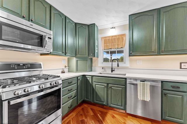 kitchen featuring hardwood / wood-style floors, green cabinets, crown molding, sink, and stainless steel appliances