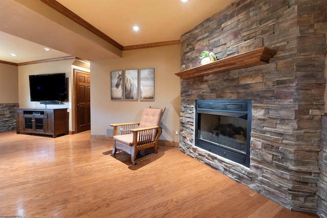 sitting room with a stone fireplace, light hardwood / wood-style flooring, and ornamental molding