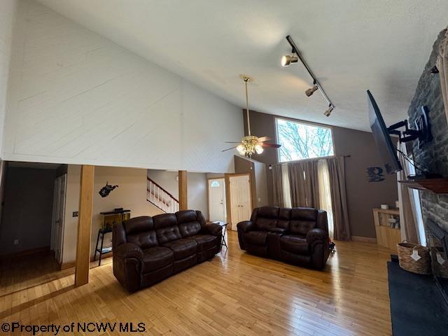 living room featuring track lighting, ceiling fan, high vaulted ceiling, a fireplace, and light hardwood / wood-style floors