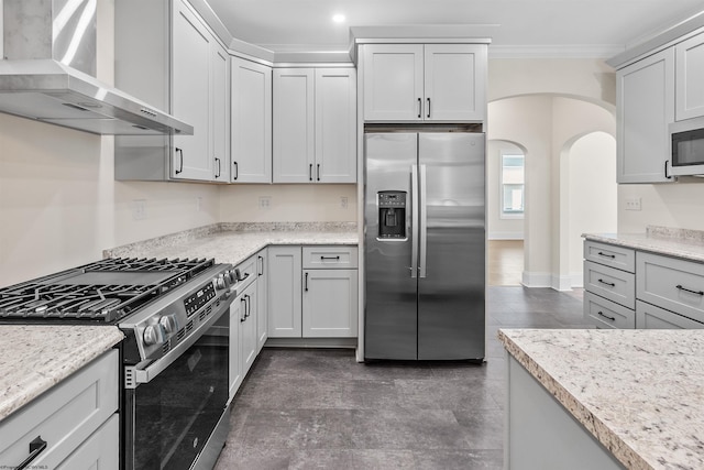 kitchen featuring light stone countertops, appliances with stainless steel finishes, ornamental molding, and wall chimney range hood