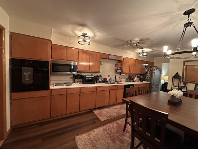 kitchen with dark wood-type flooring, black appliances, sink, ceiling fan, and decorative light fixtures