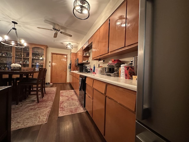 kitchen with ceiling fan with notable chandelier, dark wood-type flooring, pendant lighting, black dishwasher, and stainless steel refrigerator