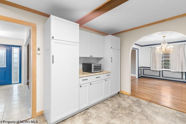 kitchen with light stone countertops, crown molding, an inviting chandelier, white cabinetry, and hanging light fixtures