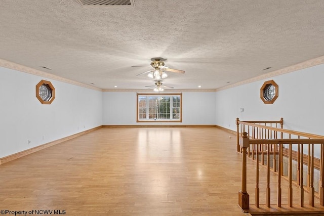 empty room featuring a textured ceiling, light hardwood / wood-style floors, ceiling fan, and ornamental molding