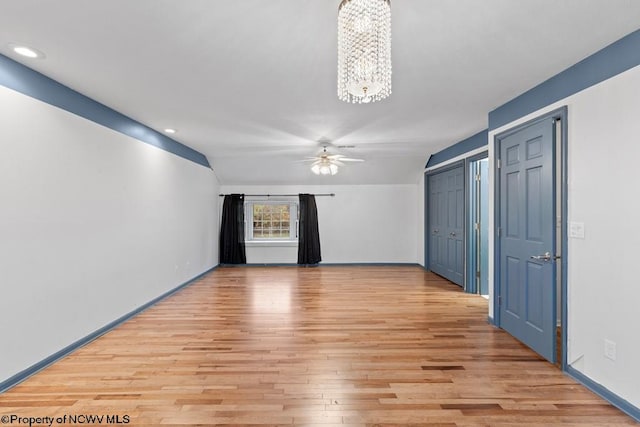 unfurnished room with lofted ceiling, light hardwood / wood-style floors, and ceiling fan with notable chandelier