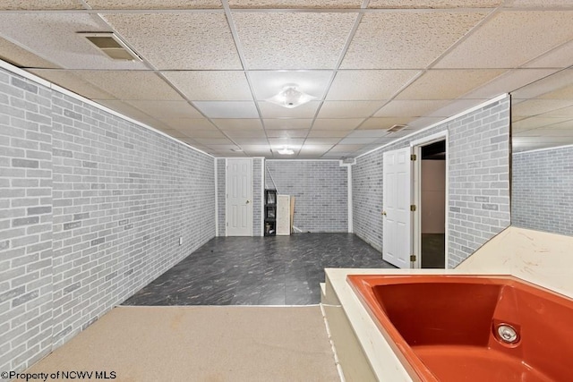 basement featuring a paneled ceiling and brick wall