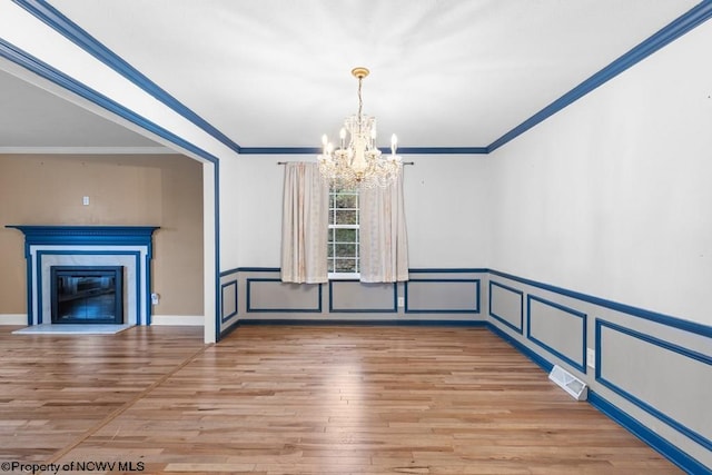 unfurnished dining area featuring hardwood / wood-style floors, a premium fireplace, ornamental molding, and a chandelier