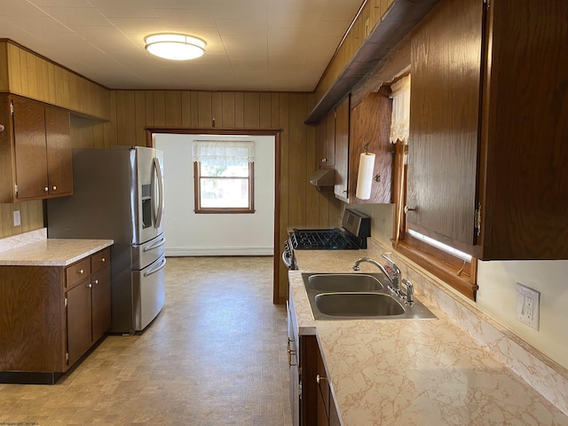 kitchen with baseboard heating, sink, wooden walls, and stainless steel appliances