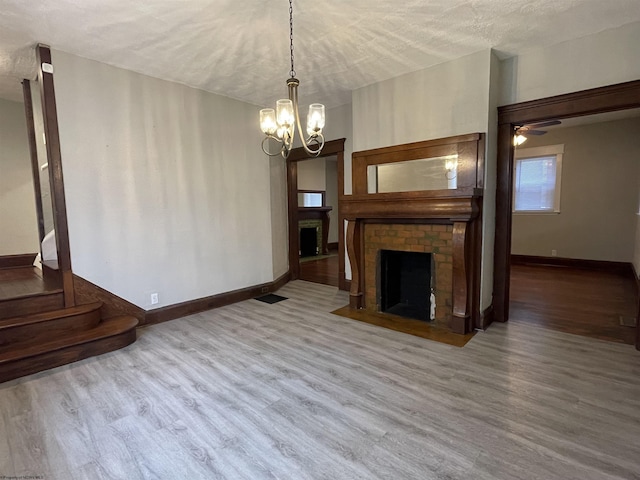 unfurnished living room featuring a fireplace, ceiling fan with notable chandelier, hardwood / wood-style floors, and a textured ceiling