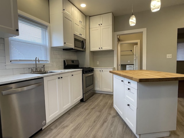 kitchen featuring decorative backsplash, appliances with stainless steel finishes, wood counters, a center island, and white cabinetry