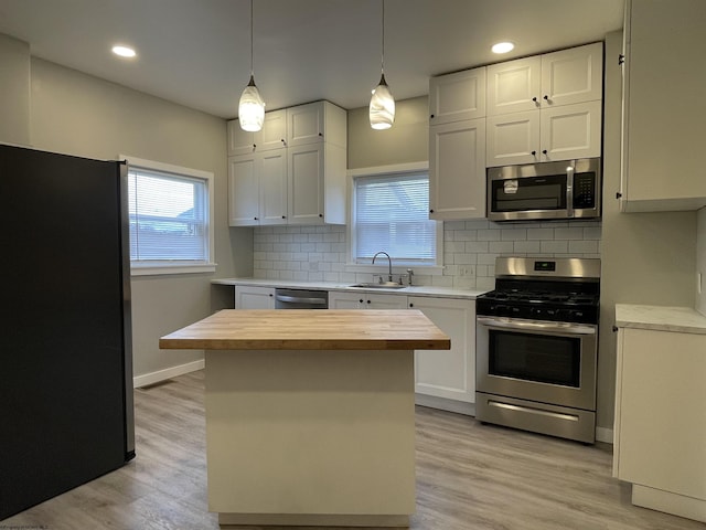 kitchen with sink, stainless steel appliances, butcher block countertops, backsplash, and white cabinets