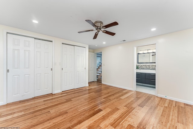 unfurnished bedroom featuring ensuite bath, ceiling fan, light hardwood / wood-style flooring, and multiple closets