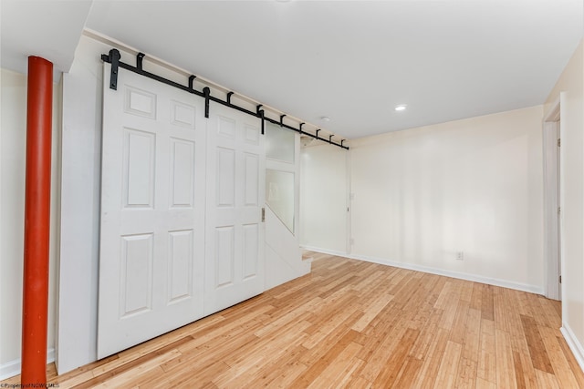 unfurnished room with a barn door and light hardwood / wood-style flooring