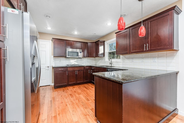 kitchen with dark stone counters, stainless steel appliances, sink, light hardwood / wood-style flooring, and hanging light fixtures