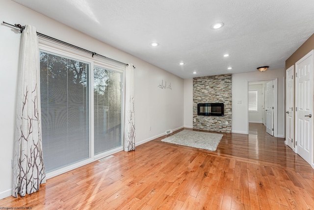 unfurnished living room featuring light wood-type flooring and a stone fireplace