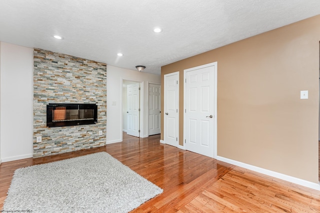 living room featuring a stone fireplace, wood-type flooring, and a textured ceiling