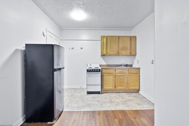 kitchen with stove, sink, stainless steel fridge, light wood-type flooring, and a textured ceiling