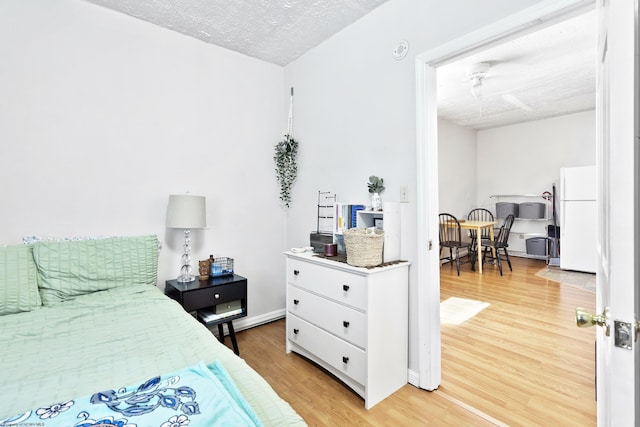 bedroom with hardwood / wood-style floors, white fridge, and a textured ceiling