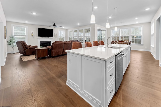 kitchen featuring white cabinetry, sink, hanging light fixtures, stainless steel dishwasher, and a kitchen island with sink