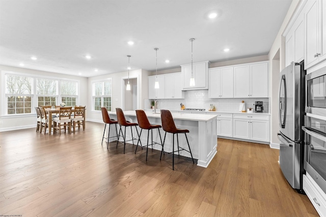 kitchen featuring white cabinets, a kitchen bar, hanging light fixtures, and a kitchen island with sink