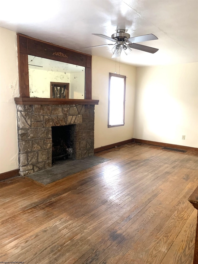 unfurnished living room with wood-type flooring, a stone fireplace, and ceiling fan