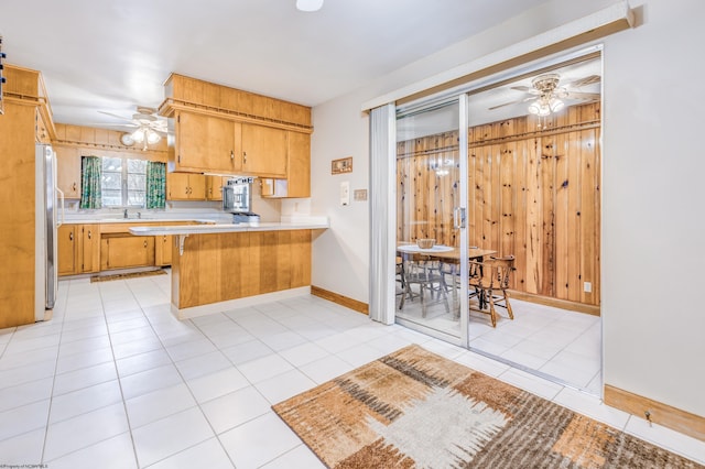 kitchen with kitchen peninsula, stainless steel fridge, light tile patterned floors, and wooden walls