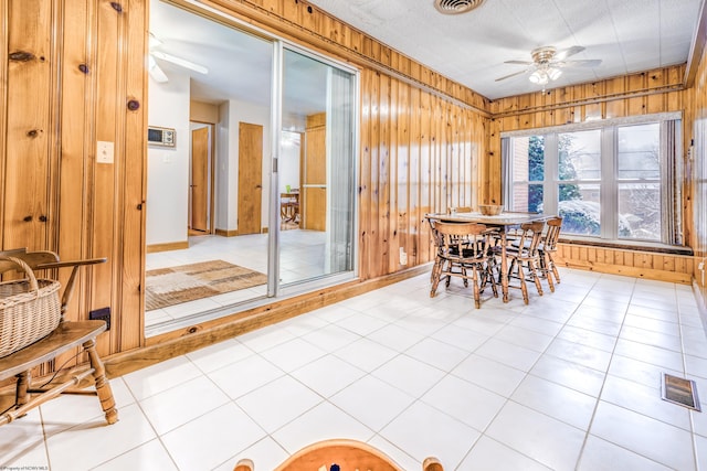 dining room featuring light tile patterned floors, a textured ceiling, ceiling fan, and wooden walls