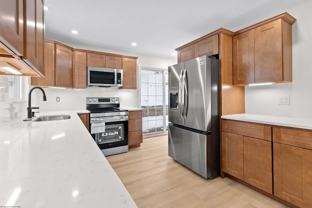 kitchen with light stone countertops, sink, appliances with stainless steel finishes, and light hardwood / wood-style flooring