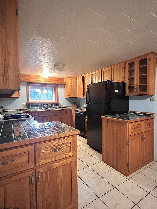 kitchen featuring tile countertops, sink, light tile patterned floors, and black appliances