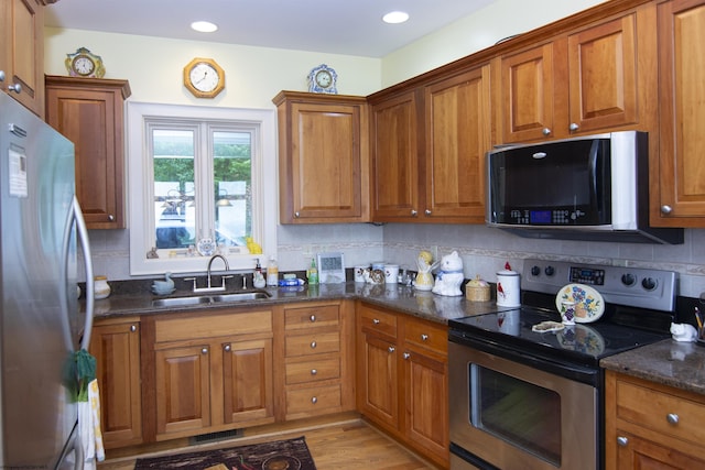 kitchen with sink, light hardwood / wood-style flooring, dark stone countertops, tasteful backsplash, and stainless steel appliances