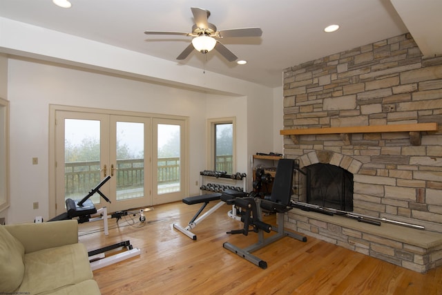 exercise room featuring a stone fireplace, ceiling fan, french doors, and wood-type flooring