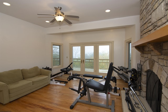 exercise area featuring a stone fireplace, ceiling fan, light hardwood / wood-style flooring, and french doors