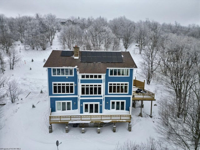 snow covered house featuring french doors, a deck, and solar panels