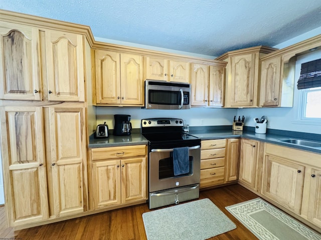 kitchen featuring a textured ceiling, stainless steel appliances, light brown cabinetry, and dark wood-type flooring