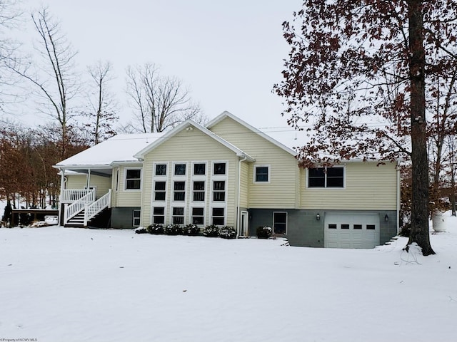 snow covered house featuring covered porch and a garage