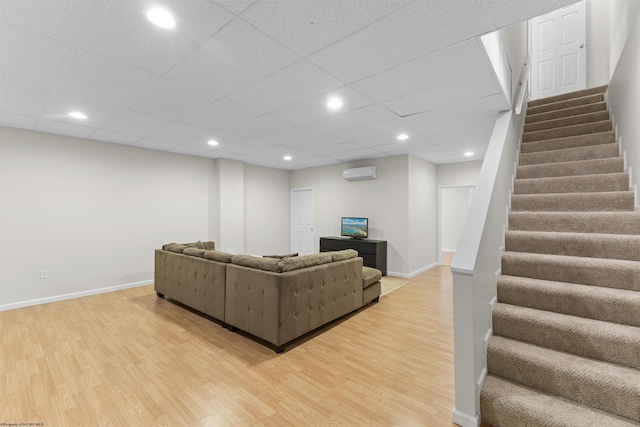 living room with a wall mounted air conditioner, a drop ceiling, and light hardwood / wood-style floors