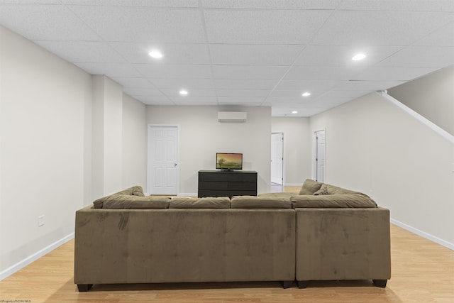 living room featuring light hardwood / wood-style floors, a wall unit AC, and a drop ceiling