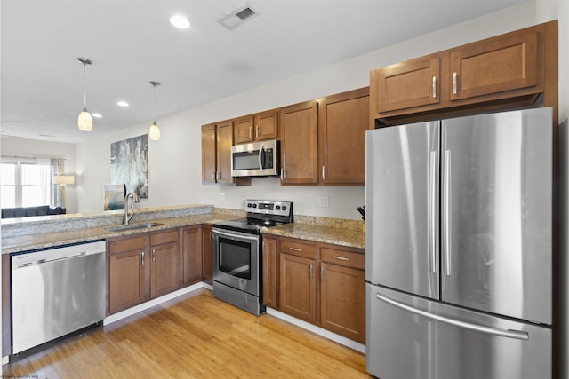 kitchen featuring hanging light fixtures, sink, appliances with stainless steel finishes, light hardwood / wood-style floors, and light stone counters