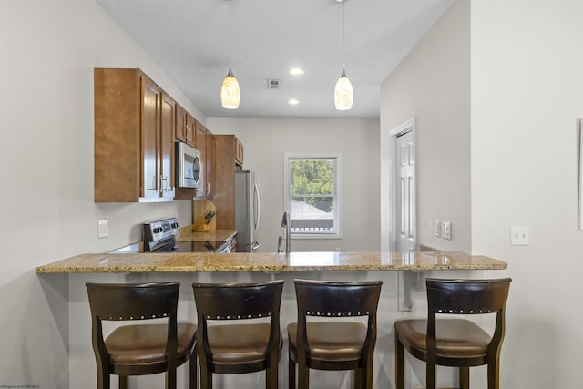 kitchen with kitchen peninsula, light stone counters, stainless steel appliances, pendant lighting, and a breakfast bar area